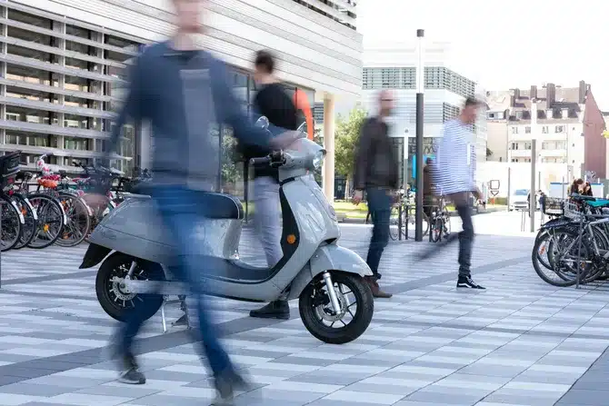 Geparkter E-Roller, Füßgänger*innen die vorbei laufen und abgestellte Fahrräder im Hintergrund.
